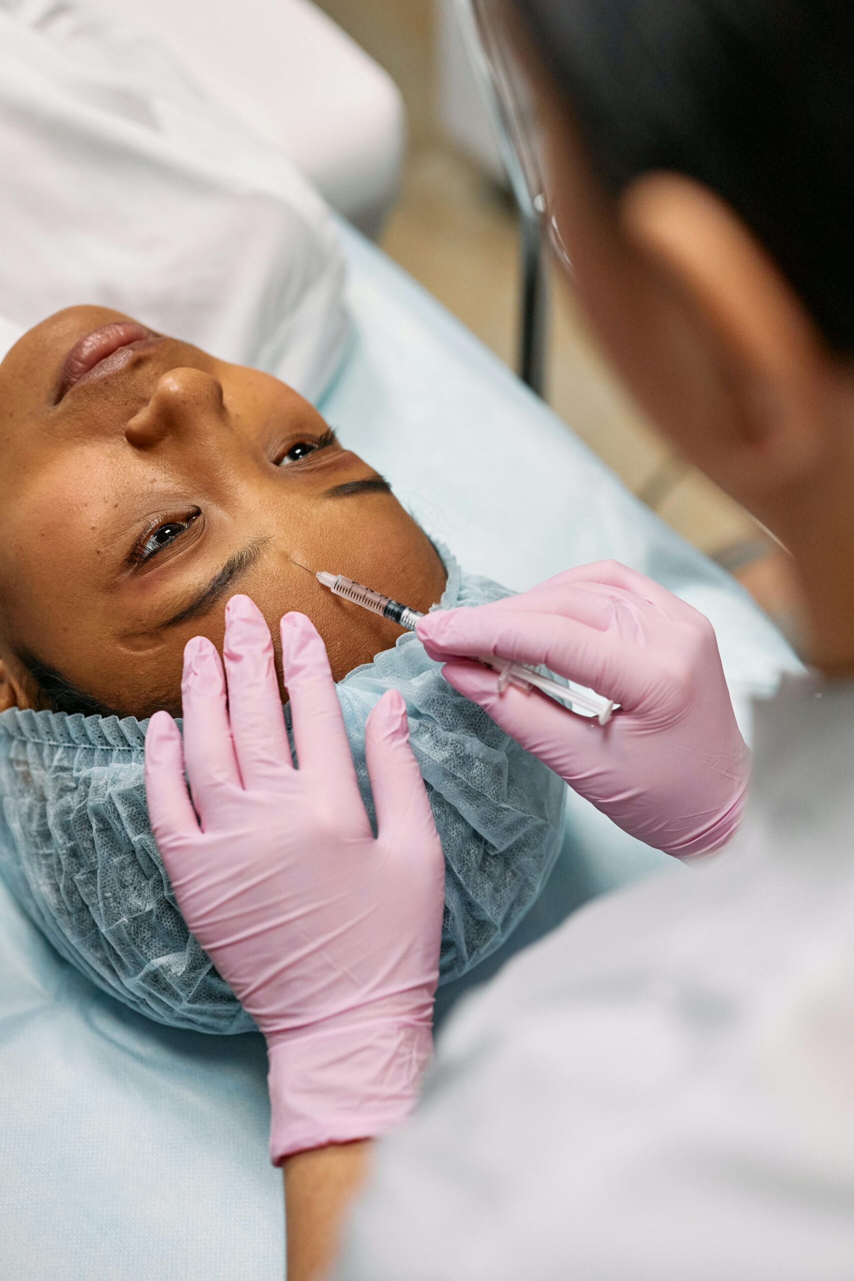 Young Black woman getting a facial injection to the forehead by a medical provider wearing pink gloves. Photo by Cottonbro on Pexels.